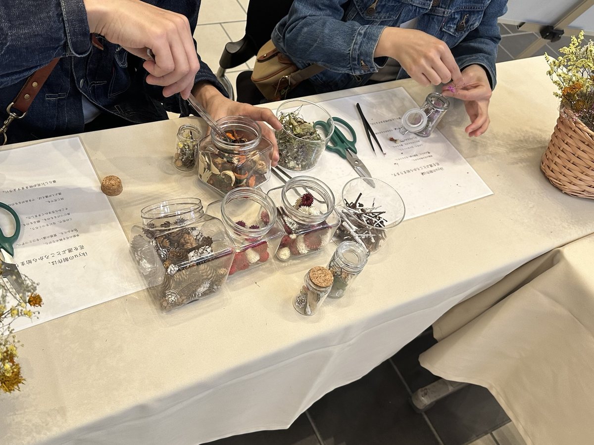 花材の瓶が並ぶテーブルで、ピンセットを手にフラワーボトルを制作する参加者の手元