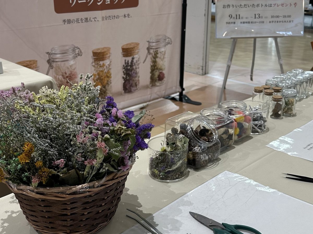花材のかご、木の実や花が入ったガラス瓶、ピンセットとハサミが並ぶ制作テーブル